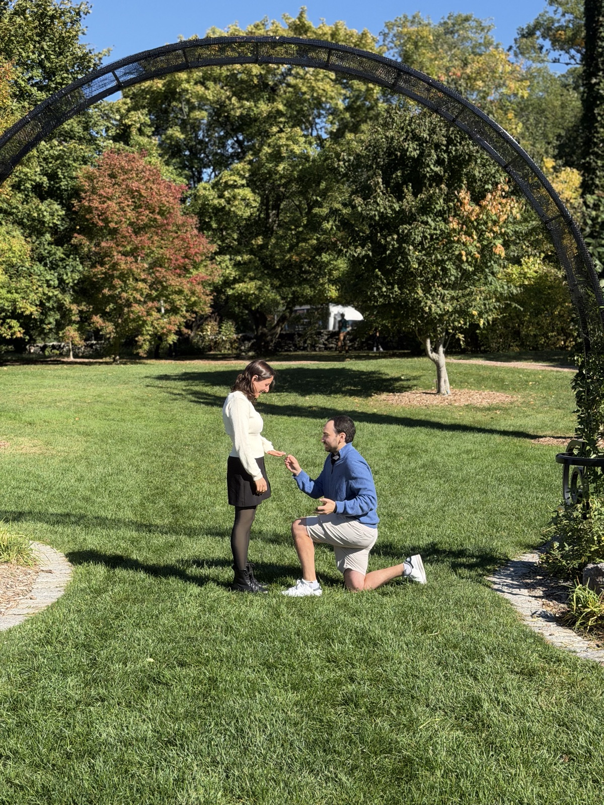 Mack proposing to Dafna beneath a garden arch in autumn